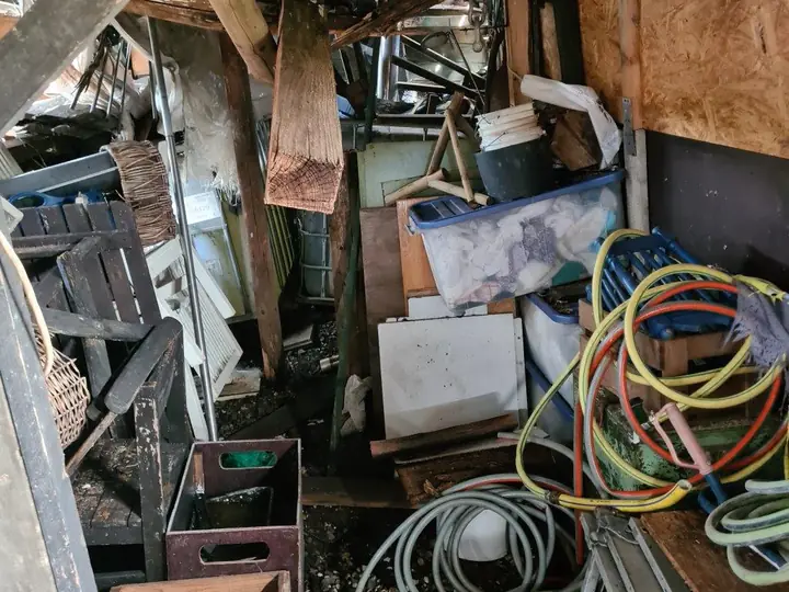 Vollgestellter Speicher mit Kisten, Schläuchen und Holz vor der Entrümpelung